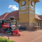 Exterior image of Dental Depot's South Tulsa dentist office with a clock tower, model train, yellow exterior, and red roof.