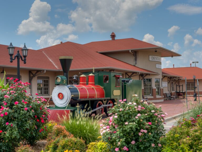 Exterior image of Dental Depot's dental office in South Oklahoma City with landscaping in the foreground and a model train and the dental clinic behind