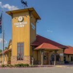 An exterior view of Dental Depot's Broken Arrow dentist office with yellow walls, a red roof, and a train station themed clock above the entrance.