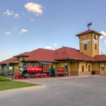 Exterior image of Dental Depot's Tulsa dentist office with a clock tower, model train, yellow exterior, and red roof.