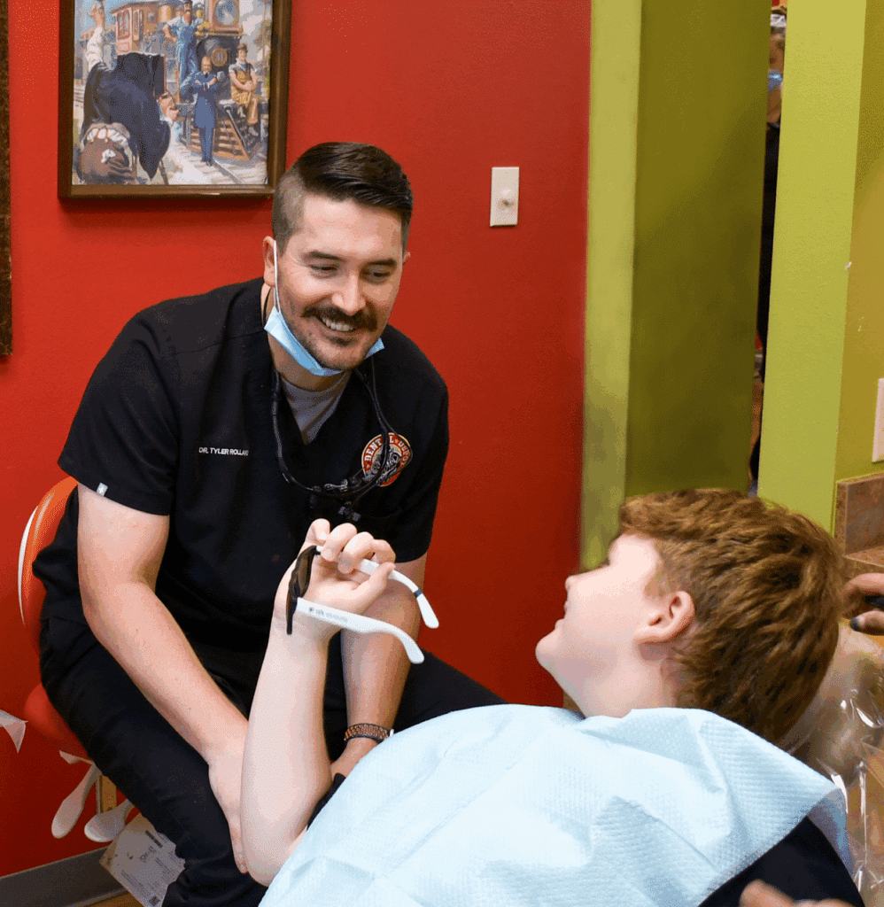 A dentist talks with a young patient while performing a dental exam and teeth cleaning.