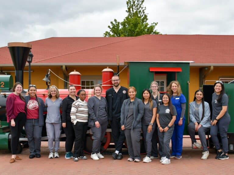 The South OKC Dental Depot dental team poses by the model train in front of the dental clinic.