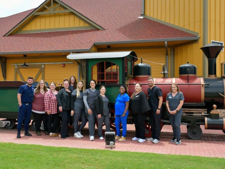 The Tulsa Hills dental team poses in front of the model train outside the Tulsa Hills dental clinic