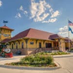 Exterior view of Dental Depot's Central Tulsa dental clinic with a model train, clock tower, and flagpole next to the yellow office.