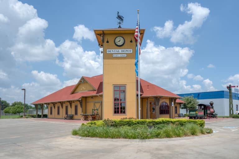 Exterior image of Dental Depot's Southwest OKC dental clinic with a flagpole, clock tower, and yellow exterior.