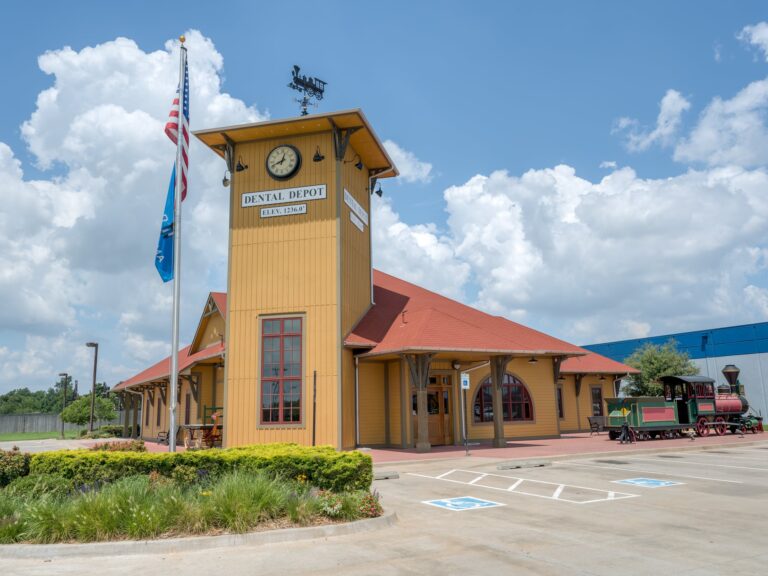 Exterior image of the Dental Depot dental clinic in Southwest OKC with a flagpole, clock tower, yellow exterior and red roof.