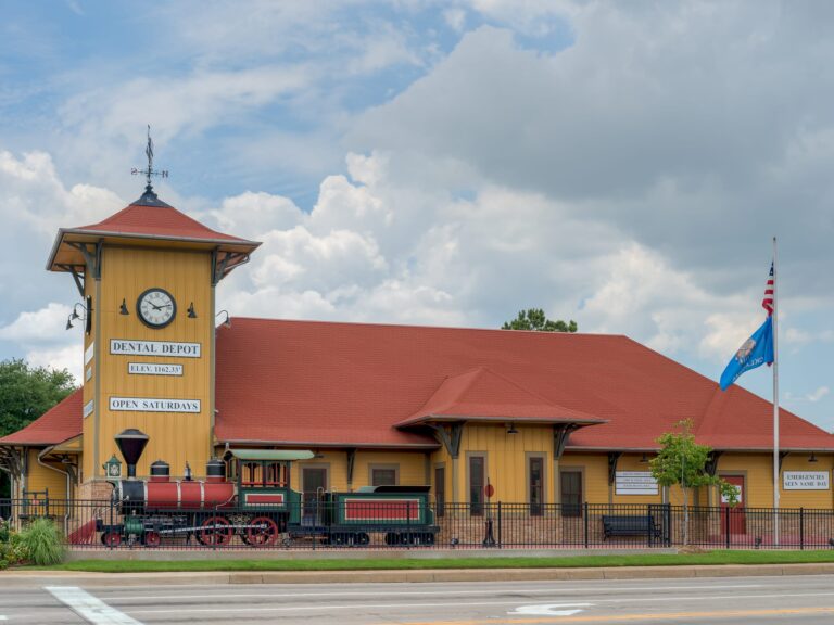 Exterior view of Dental Depot's Norman dentist office with a clock tower, model train, and yellow walls.