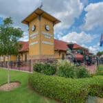 Exterior view of Dental Depot's Norman dental clinic with nice landscaping in the foreground and a building with a clock tower and a yellow exterior in the background.