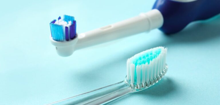 A manual and an electric toothbrush laying down on a blue background