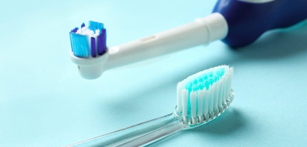 A manual and an electric toothbrush laying down on a blue background