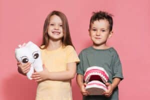 A smiling boy and a girl with healthy teeth hold a toy tooth in their hands on an isolated background.