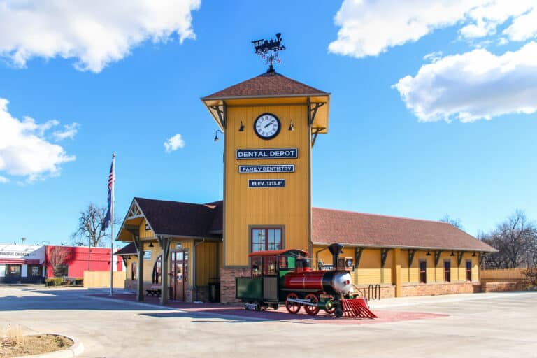 Del City Dental Clinic's exterior view with yellow walls and a large model train in front.