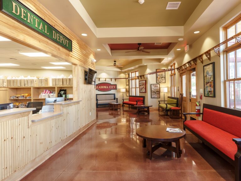 Waiting room at Dental Depot's NW 63rd St Oklahoma City Dental office with red furniture, light colored wood, and train décor.