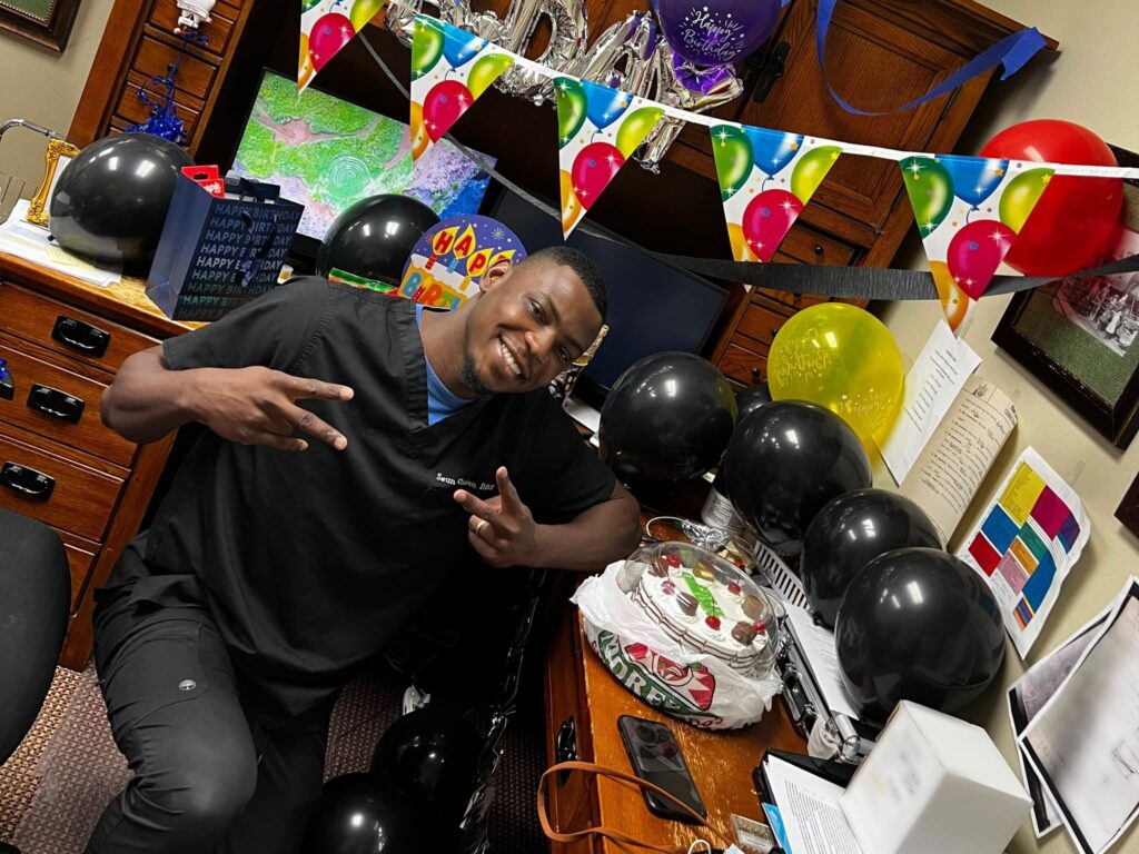 Dr. Olaniran poses at his desk that is decorated with balloons and streamers for his birthday