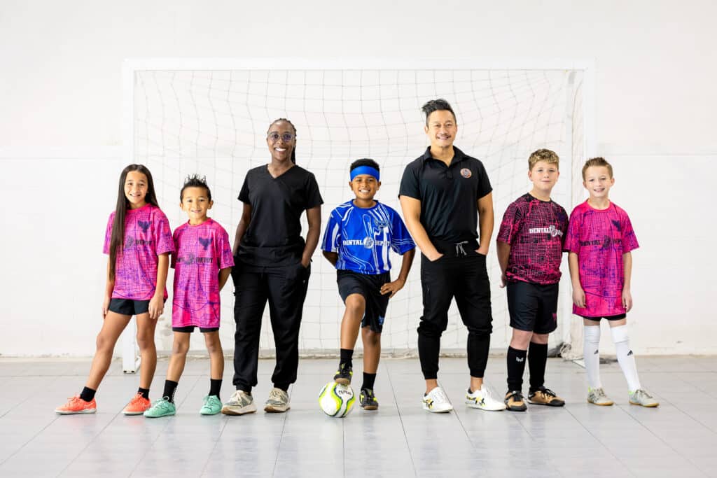 Kids wearing Invicto Futsal jerseys sponsored by Dental Depot stand next to dentists and pose in their gear.