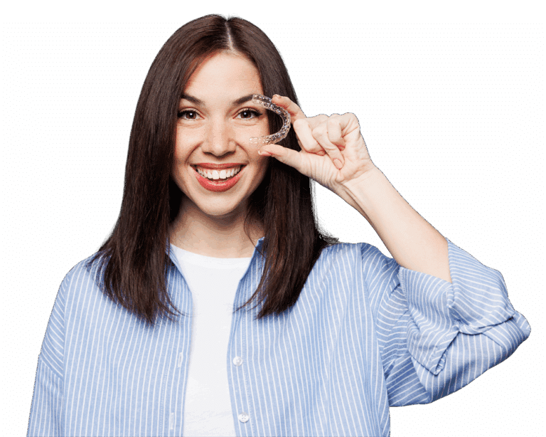 A young woman smiles while hold Invisalign clear aligners in front of her face.