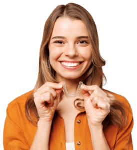 Brunette woman in an orange shirt holds an Invisalign aligner and smiles at the camera.