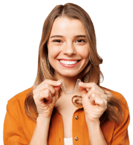 A young woman in an orange shirt smiles widely while holding Invisalign aligners