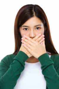 Image of a young woman hiding her teeth for the dark spots on teeth blog post.