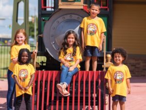 Kids wearing yellow Dental Depot t-shirts sit and smile for the camera in front of a train outside the dental office.