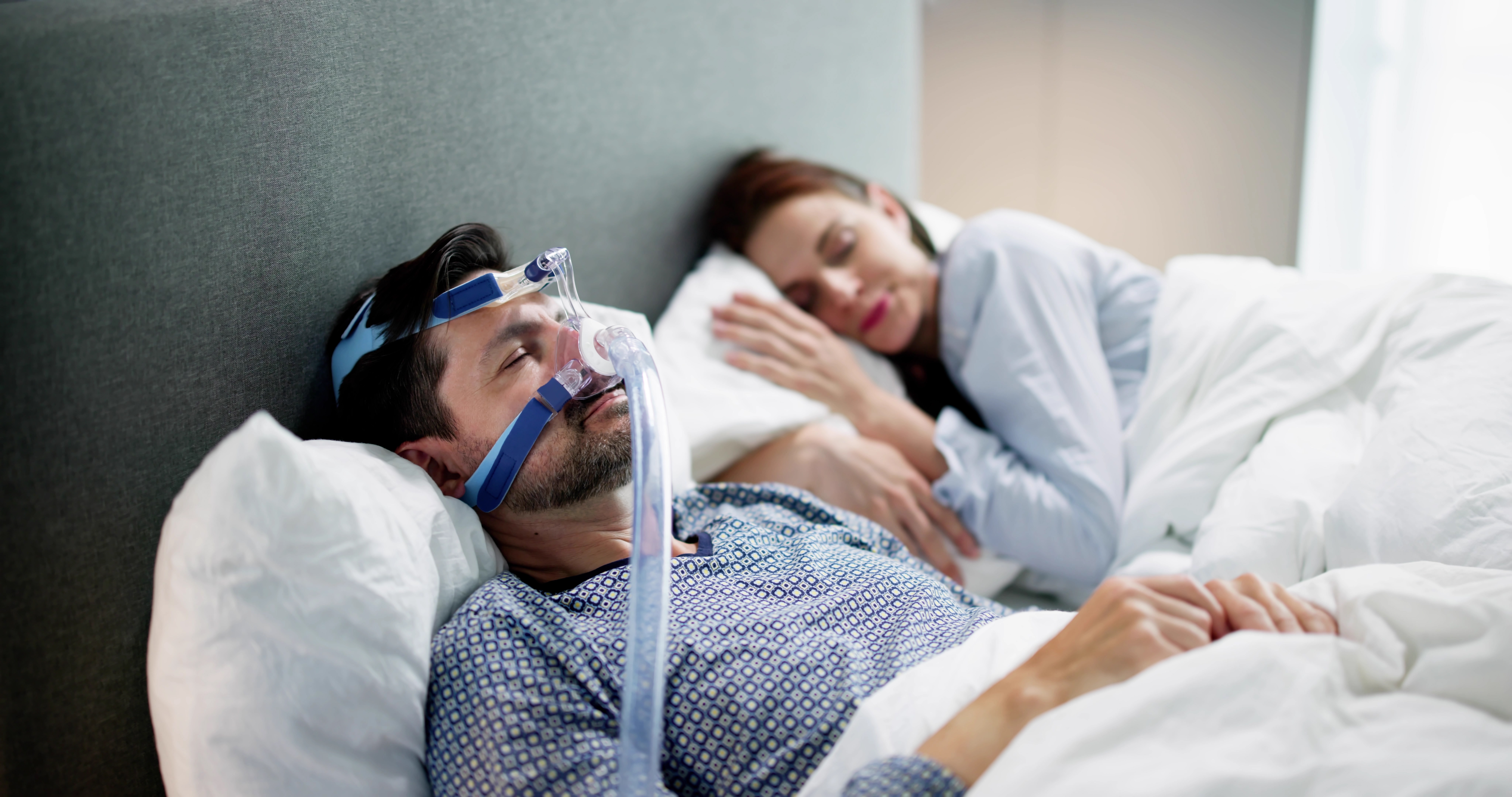 Man in sleep apnea mask sleeps on his back next to wife.