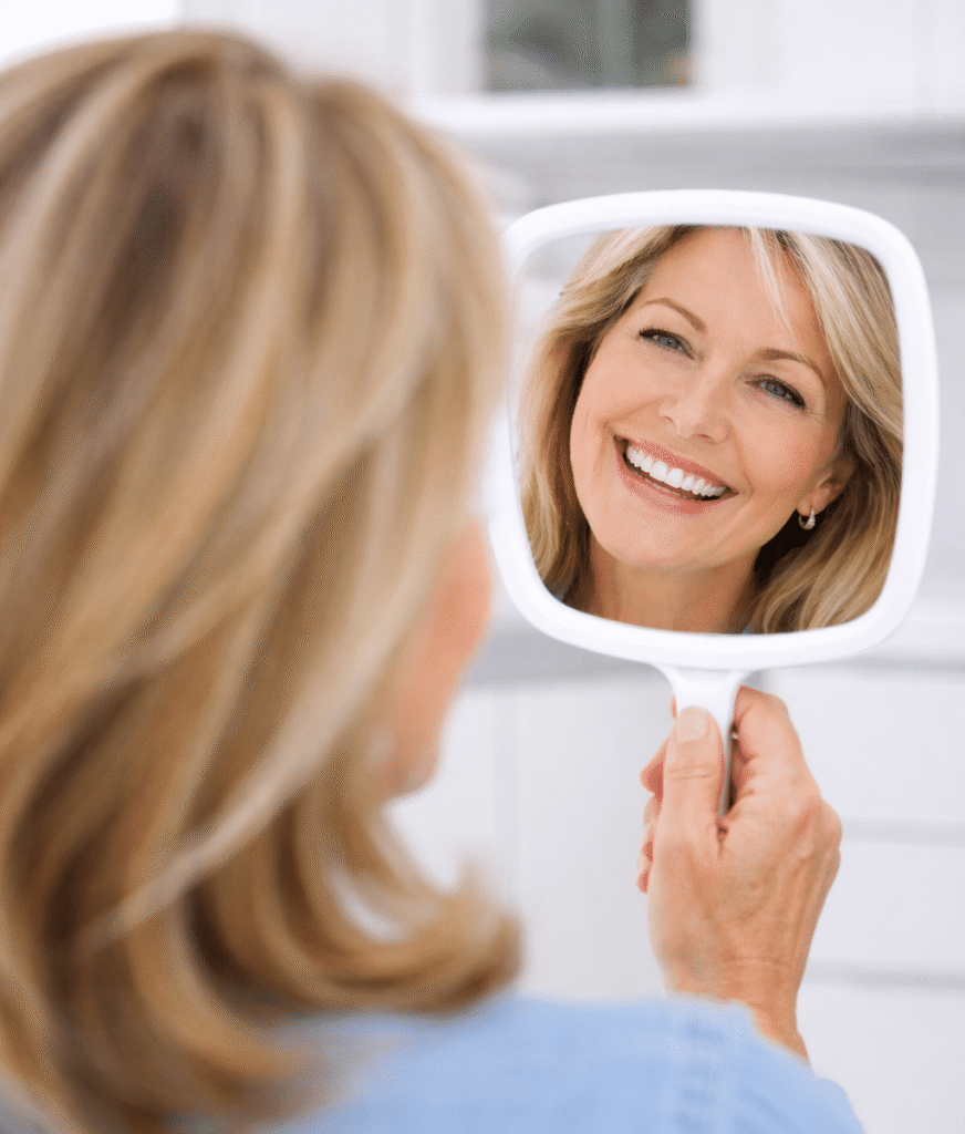 Woman smiling into a mirror after receiving dental implants at Dental Depot