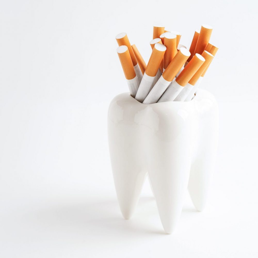 A model tooth on a white background holds a bundle of cigarettes'