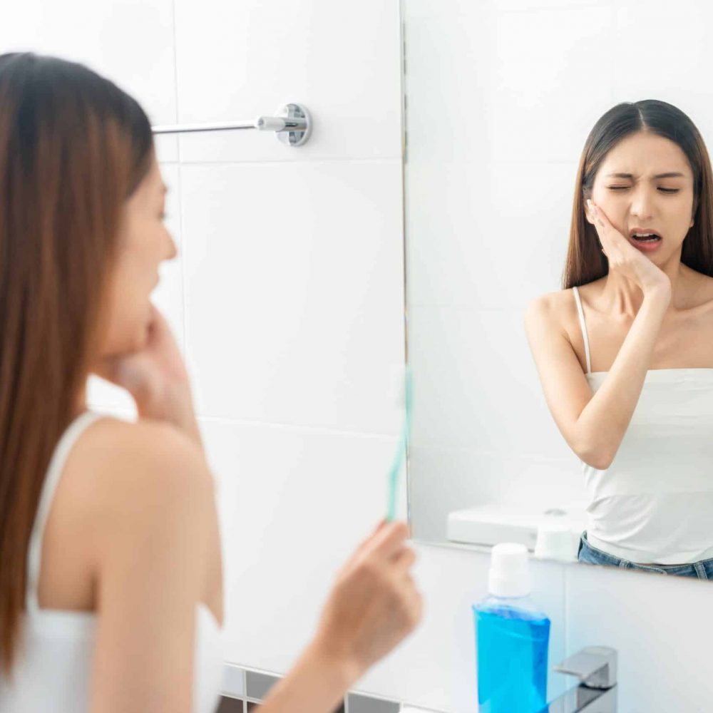 Asian woman puts her hand on her mouth and feels toothache because of tooth decay.