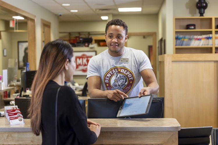 A young man helps a lady with electronic check in at dental depot